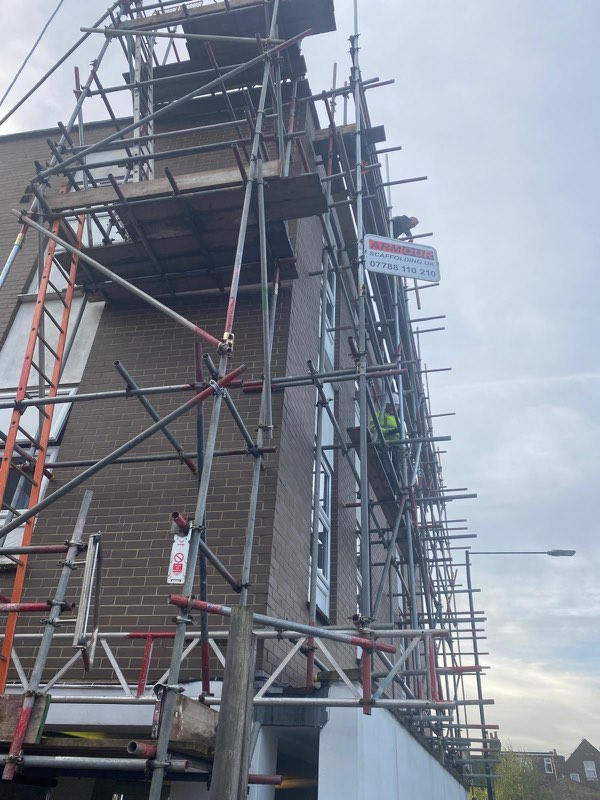Tall corner of a brick block of flats with full-height scaffold and an Armour board