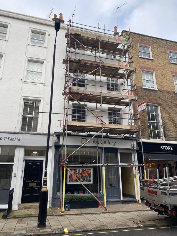 Tall narrow townhouse above a gallery shopfront with scaffold and yellow ground-floor protection