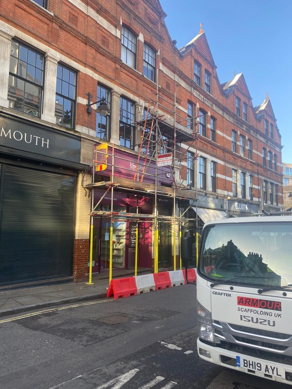 Red-brick Victorian parade with scaffold at the shopfront, barriers on the road and an Armour lorry