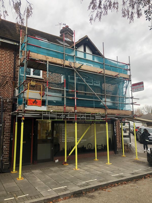 Corner shop-fronted property wrapped in sheeted scaffold on yellow props